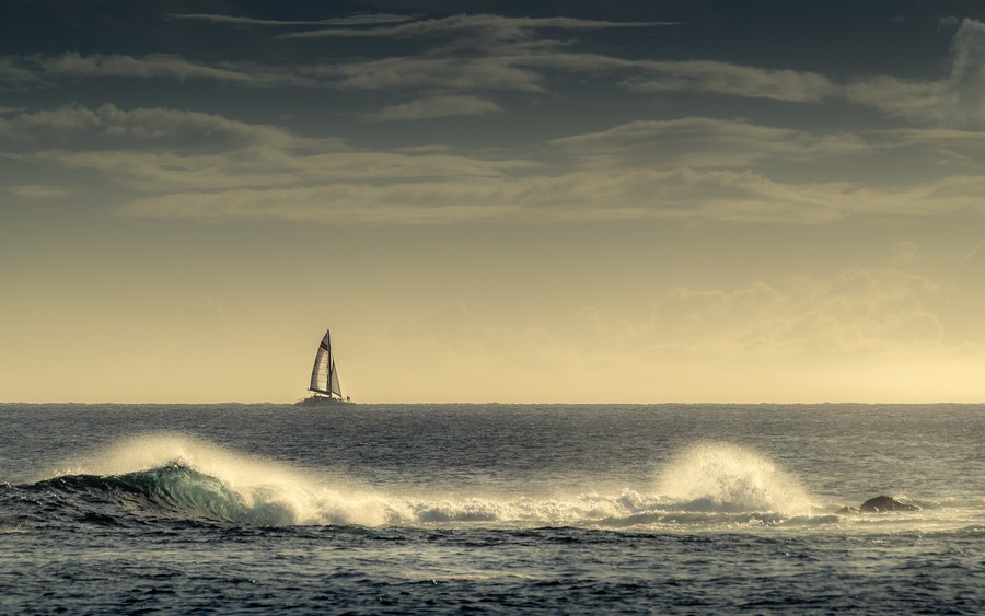 Horizon Elegance: Sunset Sailboat Over Turquoise Waves